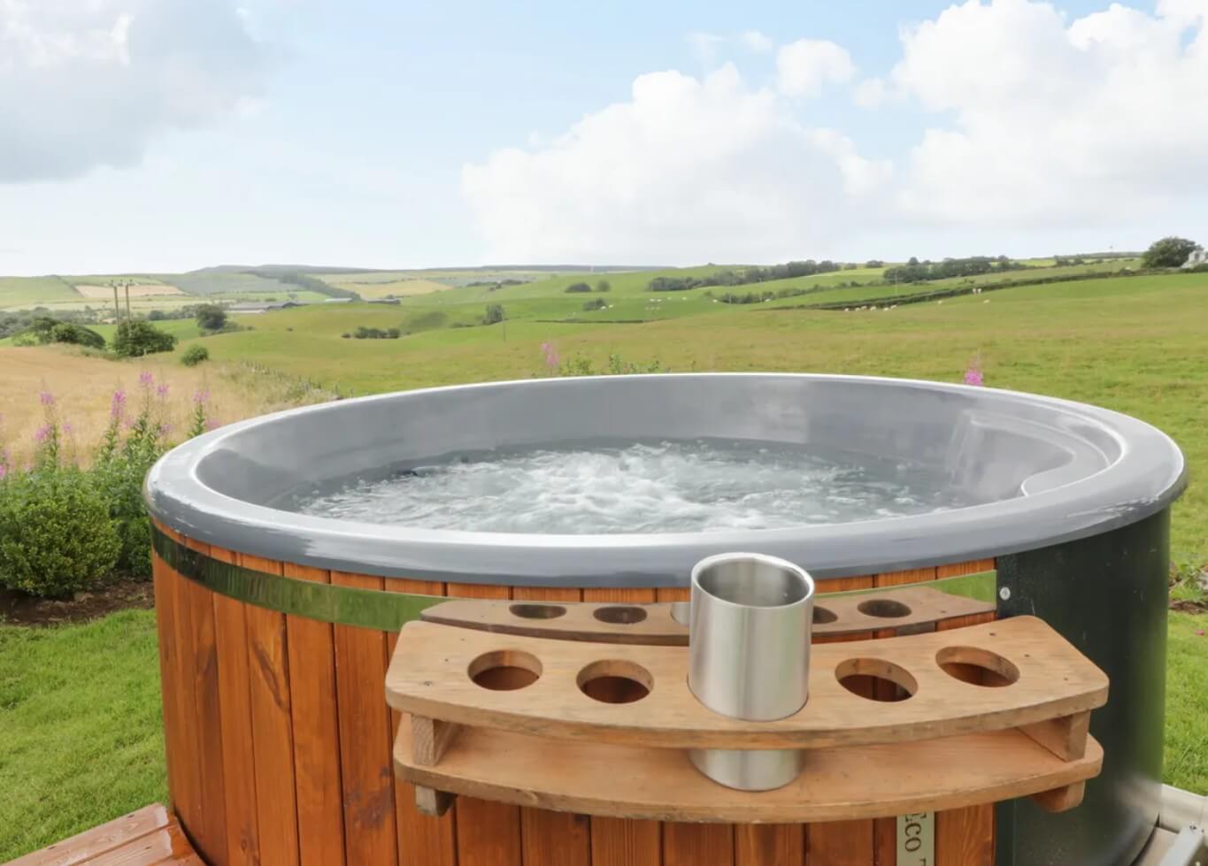 A cosy Straiton cottage with a steaming private hot tub on a wooden deck, set amidst the rolling green Ayrshire countryside.
